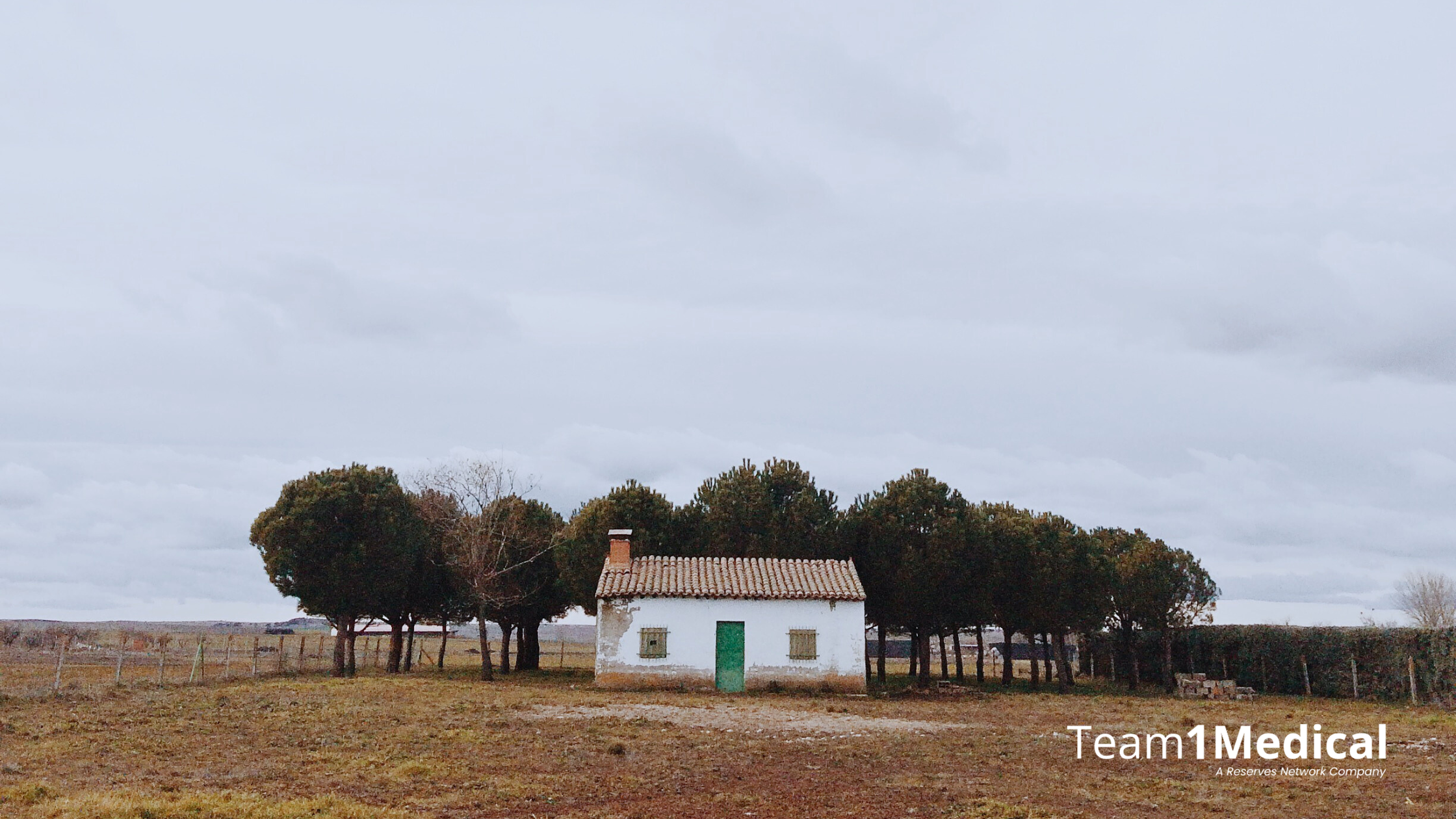 a house in a rural area on farm land, the grass is brown and bare, large gray sky