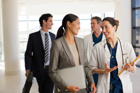 Healthcare professionals in lab coats and healthcare admins in suits walking through clinic talking